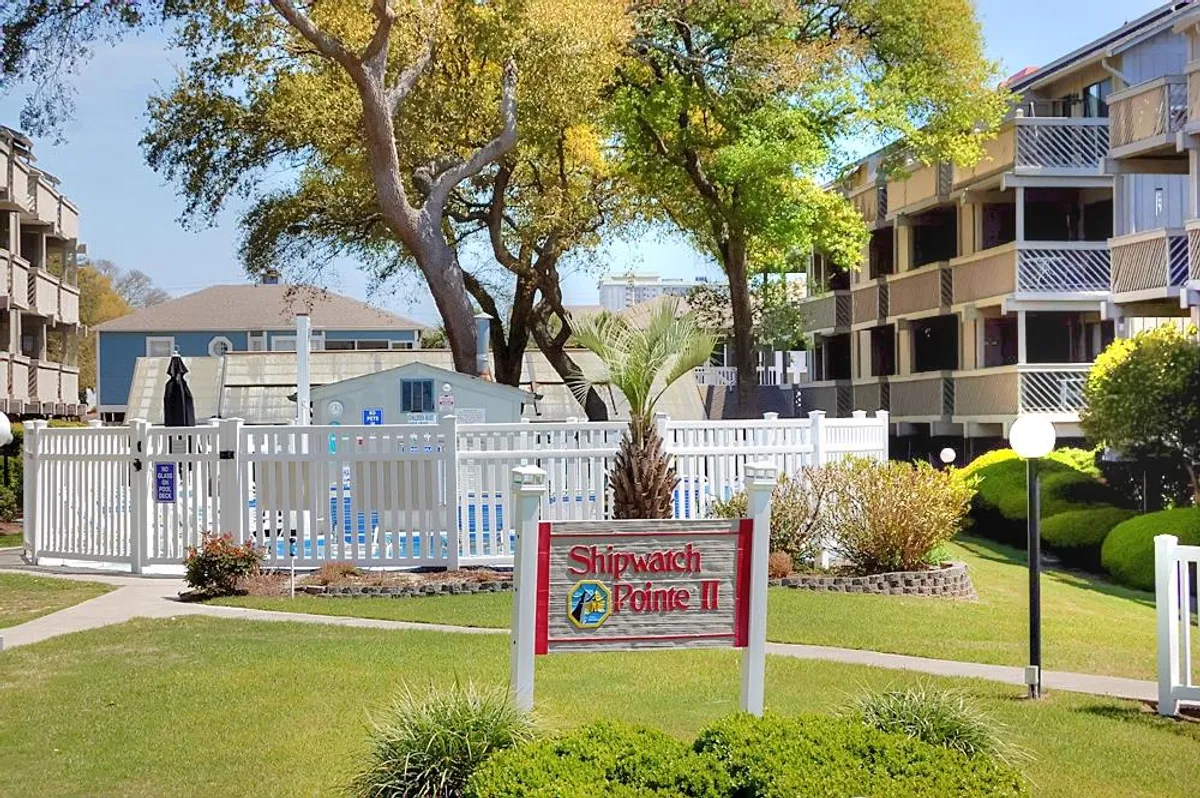 The image features a sparkling swimming pool surrounded by landscaped gardens and the building facade, with visible signage. Lounge chairs offer space for relaxation, and the leisurely mood suggests year-round enjoyment of amenities like swimming or sunbathing, even in winter's mild climate.