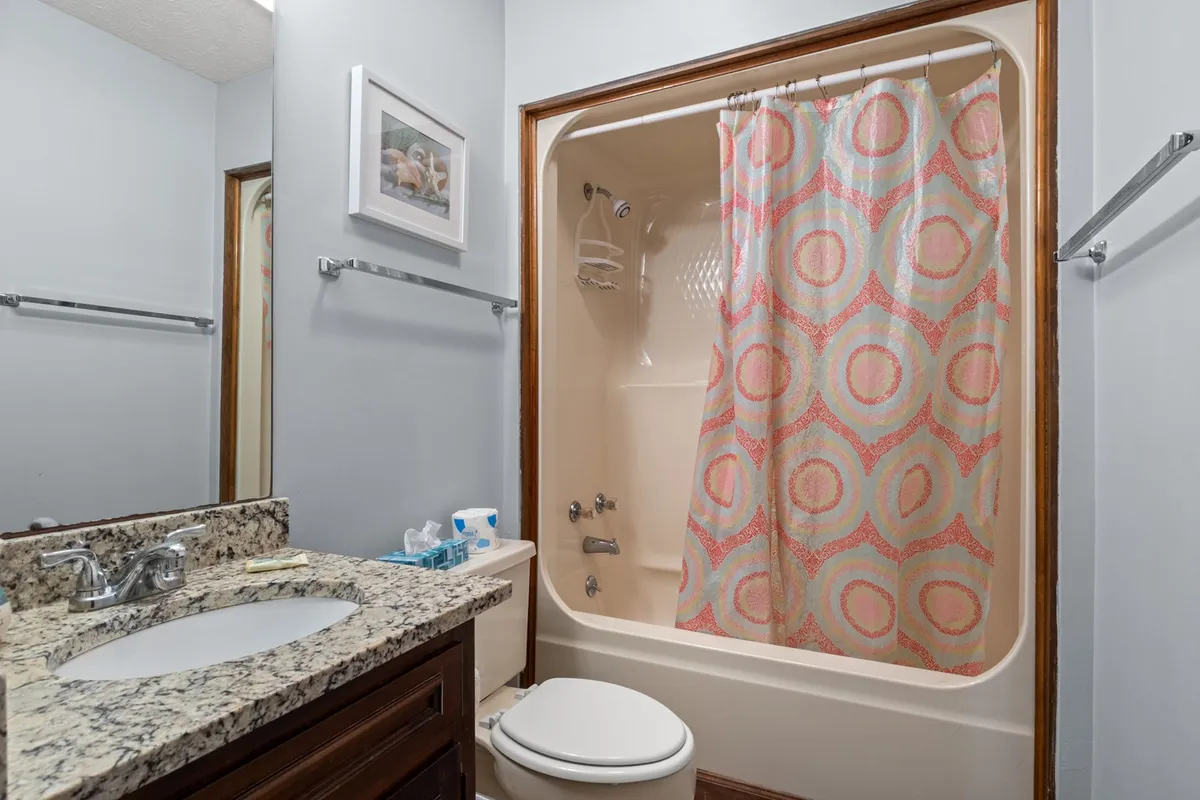 This cheerful bathroom features a granite countertop, a colorful shower curtain, and framed artwork. The space is bright and thoughtfully designed for both morning routines and evening relaxation.