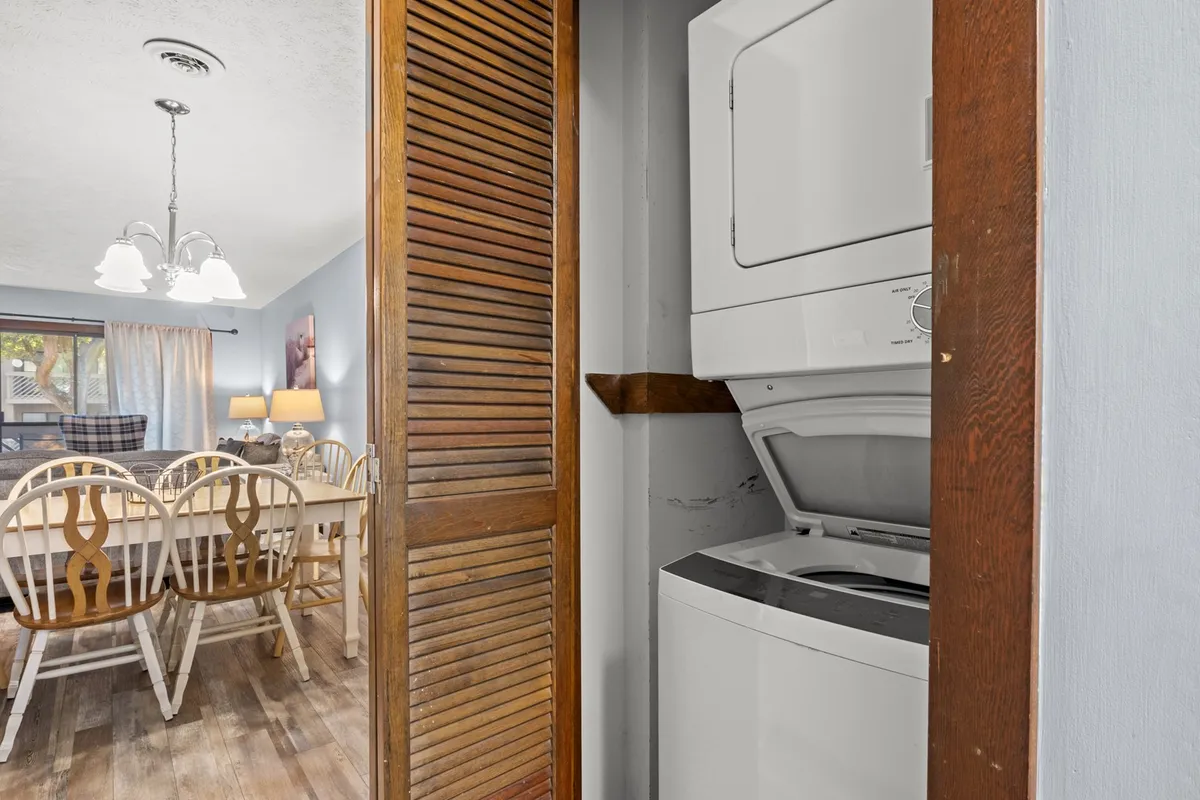 A view of the inviting dining area featuring a sturdy dining table beneath a modern light fixture, with a washing machine subtly visible in the background. The table is central, suggesting a space for family meals, planning, and conversation.
