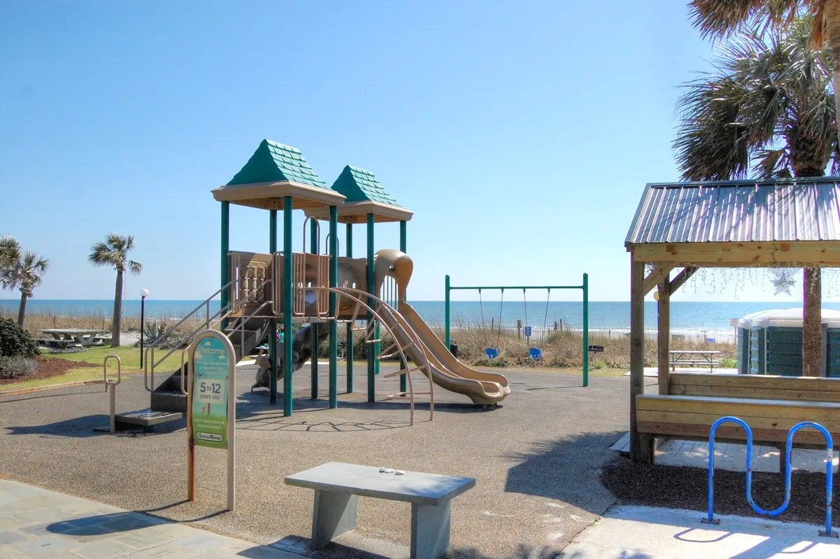 A vibrant oceanside playground with swings and a picnic area, set against a backdrop of the ocean. Children can be seen playing while families gather for picnics or simply enjoy the fresh air and views.